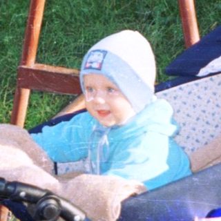 Baby in a stroller sits outdoors near a fence.