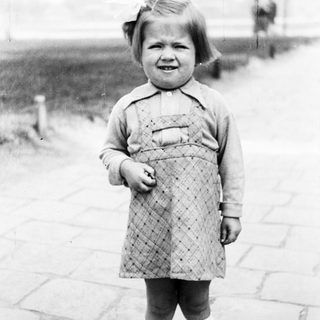Young child stands outdoors in a patterned dress and socks.