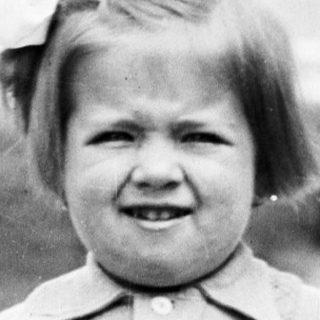 Young child stands outdoors in a patterned dress and socks.