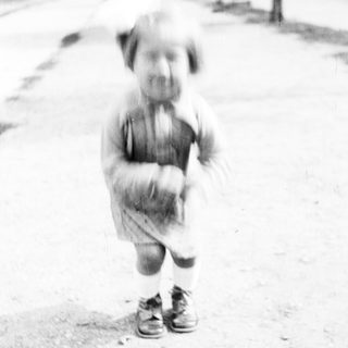 Black and white photo shows a young child standing outdoors.