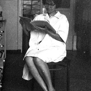 Woman in white shirt sits reading, appearing thoughtful.