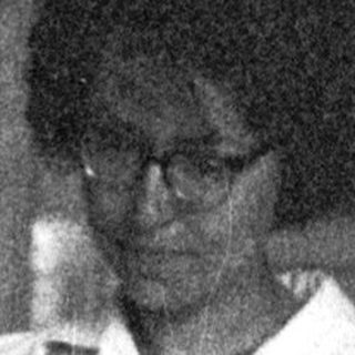 Woman in white shirt sits reading, appearing thoughtful.