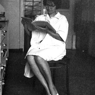 Woman in white shirt sits reading, appearing thoughtful.