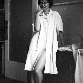 Woman in lab coat seated, appearing relaxed in a room.