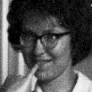 Woman in lab coat seated, appearing relaxed in a room.