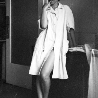 Woman in lab coat seated, appearing relaxed in a room.