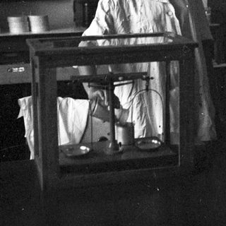 Woman in lab coat using a balance scale.