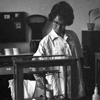 Woman in lab coat using a balance scale.