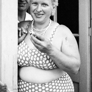 Woman in a polka dot swimsuit smiles near a doorway.