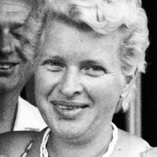 Woman in a polka dot swimsuit smiles near a doorway.