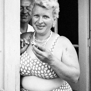 Woman in a polka dot swimsuit smiles near a doorway.