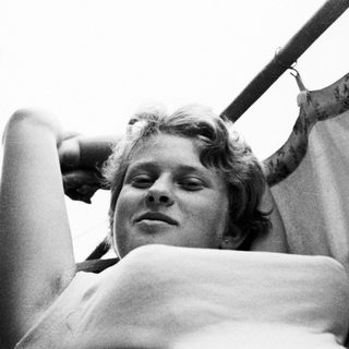 Here's a brief summary of the image: Woman reclines with eyes closed, hand behind head.