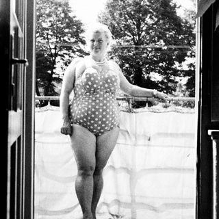 Woman in a vintage swimsuit stands in a doorway.