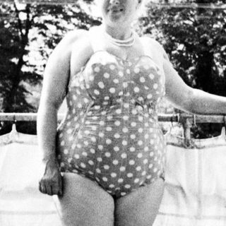Woman in a vintage swimsuit stands in a doorway.