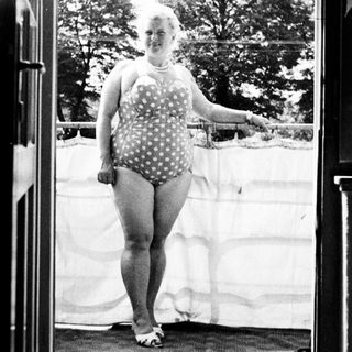 Woman in a vintage swimsuit stands in a doorway.
