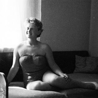 Woman in a vintage swimsuit sits on a couch.