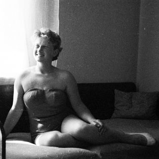 Woman in a vintage swimsuit sits on a couch.