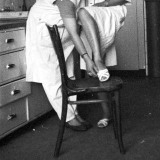 Here's a brief summary of the image: Woman in uniform assists someone with putting on shoes.