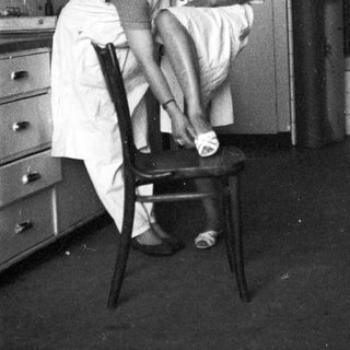 Here's a brief summary of the image: Woman in uniform assists someone with putting on shoes.