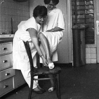 Here's a brief summary of the image: Woman in uniform assists someone with putting on shoes.