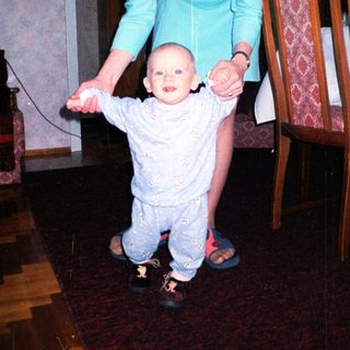 Baby takes first steps with support from a woman.