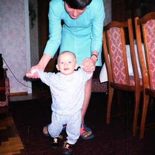 Baby takes first steps with support from a woman.