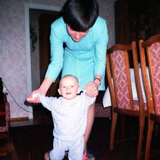 Baby takes first steps with support from a woman.