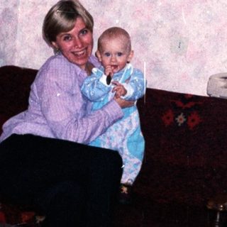 Woman holding baby, seated on a floral couch.