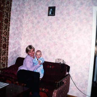 Woman holding baby, seated on a floral couch.