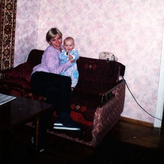 Woman holding baby, seated on a floral couch.