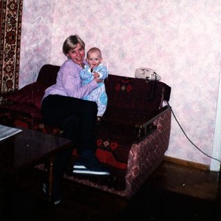 Woman holding baby, seated on a floral couch.