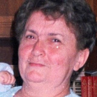 Woman holds baby indoors, standing near furniture and cabinets.