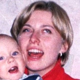 Woman holds baby on a red couch in a home.