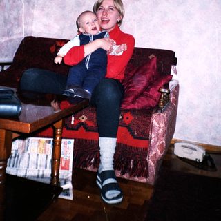 Woman holds baby on a red couch in a home.