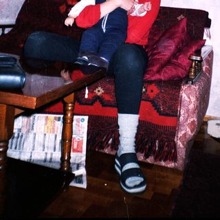Woman holds baby on a red couch in a home.