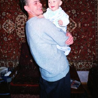 Man holds baby, both smiling, against a patterned rug.