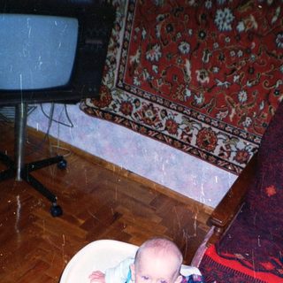 Baby sits in a seat, looking at the camera.