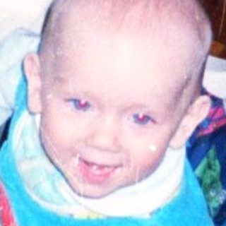 Baby sits in a seat, looking at the camera.
