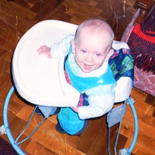 Baby sits in a seat, looking at the camera.