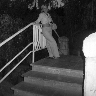 Woman stands on steps at night, holding a bag.