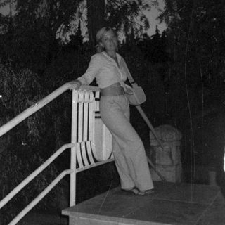 Woman stands on steps at night, holding a bag.