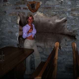 Woman stands near mounted animal head in a rustic room.