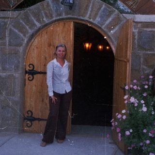 Woman stands before a stone building with an arched entrance.