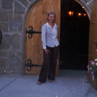 Woman stands before a stone building with an arched entrance.