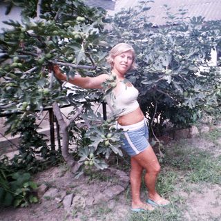Woman stands near a tree with unripe figs in a yard.