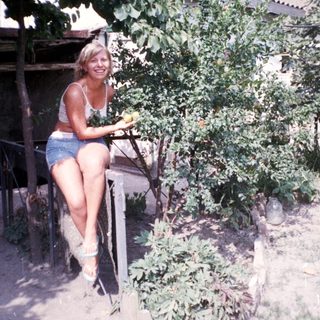 Woman poses by a tree in a yard.