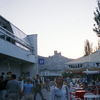 Person stands on a street with a cafe and people.