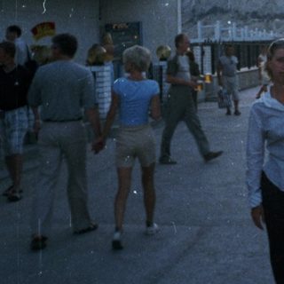 Person stands on a street with a cafe and people.