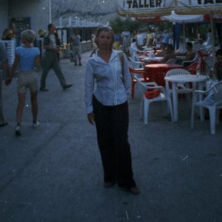 Person stands on a street with a cafe and people.