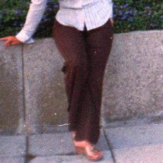 Woman stands near a wall and car in a garden.